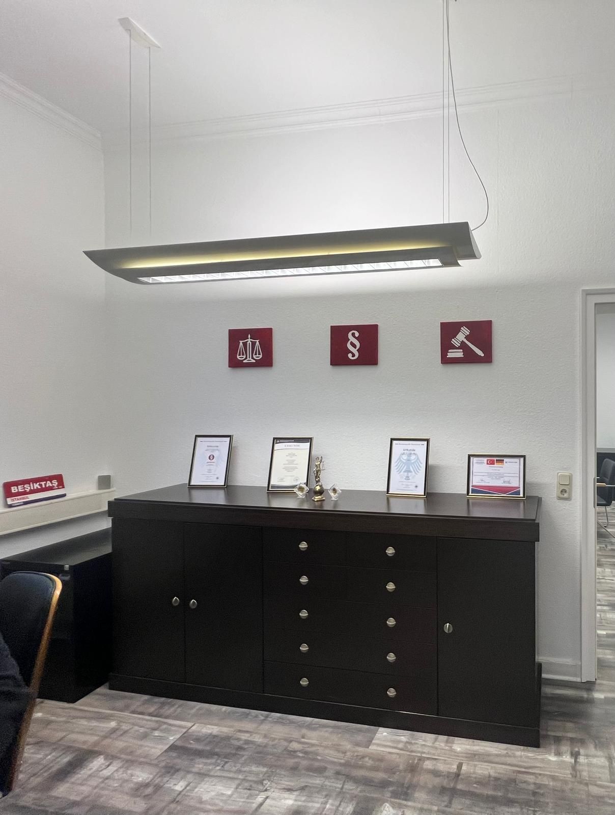 SERGIN Consulting ofisi: koyu renkli dolap, çerçeveli belgeler ve bordo duvar panoları