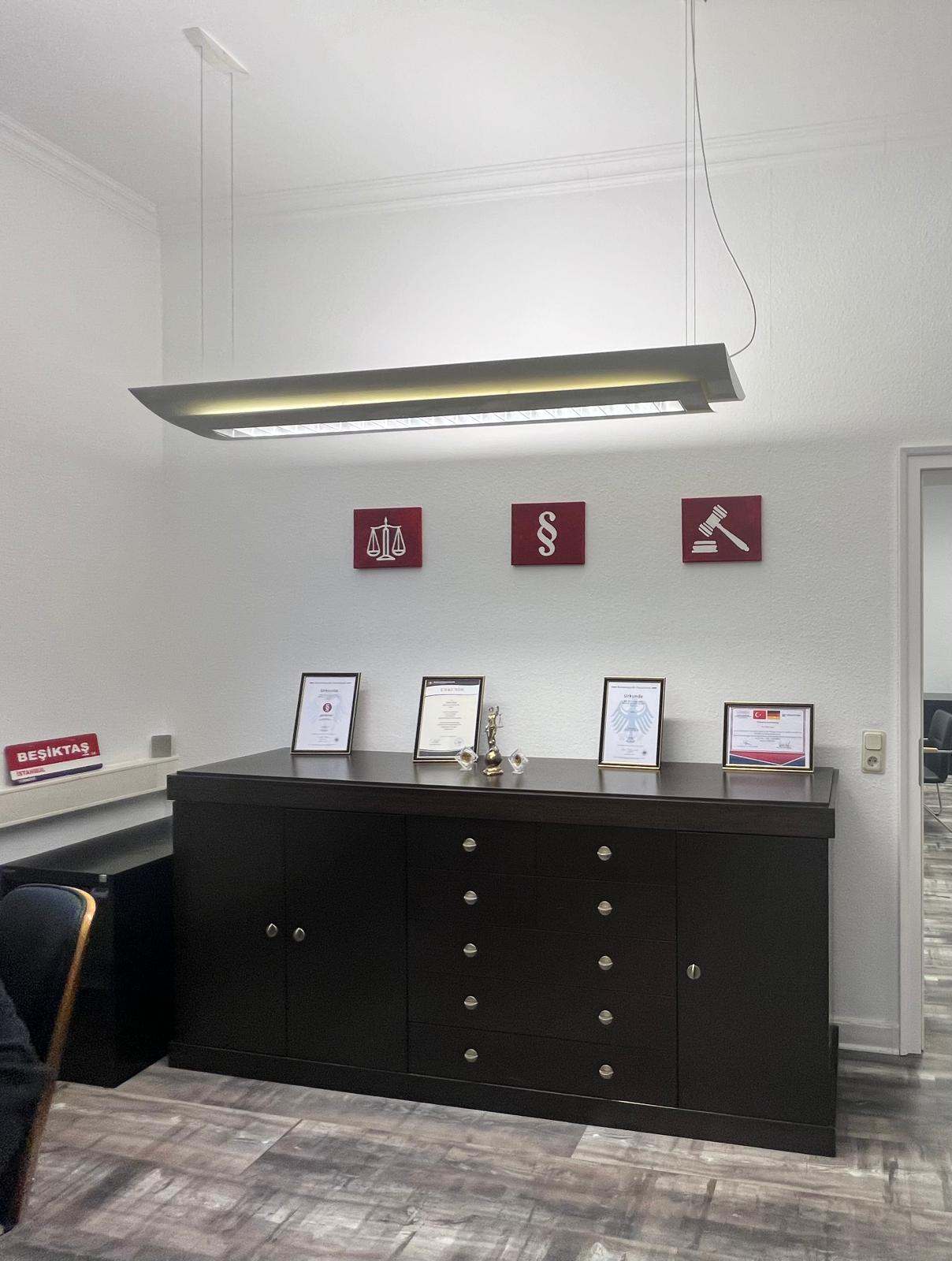 Koyu renkli dolap, çerçeveli belgeler ve üç bordo duvar panosu bulunan ofis